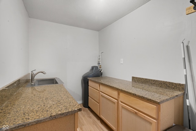 kitchen with stone counters, light brown cabinetry, light wood-type flooring, and sink