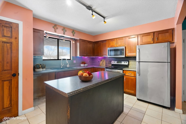 kitchen with track lighting, sink, light tile patterned floors, a kitchen island, and stainless steel appliances