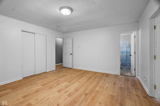 unfurnished bedroom featuring ensuite bath, a closet, light hardwood / wood-style floors, and a textured ceiling