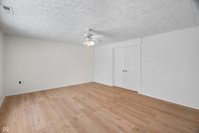 empty room featuring light wood-type flooring, ceiling fan, and brick wall