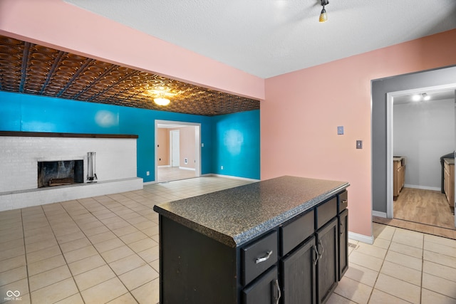 kitchen with a textured ceiling, a center island, a brick fireplace, and light tile patterned flooring