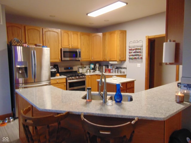 kitchen with light wood-type flooring, stainless steel appliances, a breakfast bar area, and sink