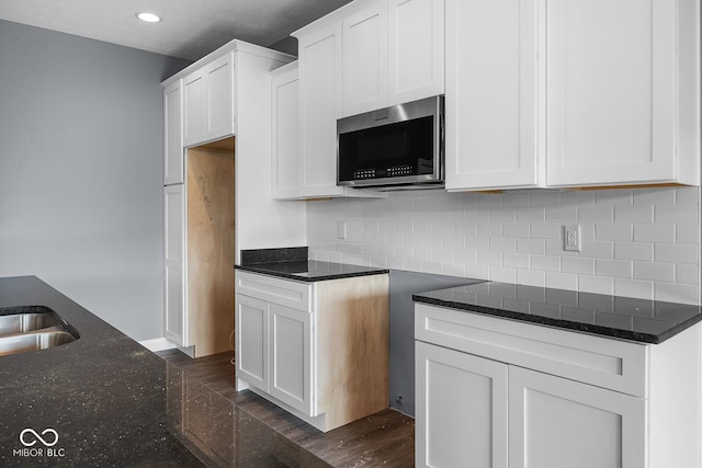 kitchen featuring tasteful backsplash, stainless steel microwave, white cabinets, and dark stone countertops