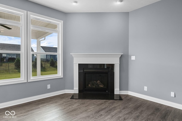 unfurnished living room featuring ceiling fan, a fireplace with raised hearth, dark wood-style flooring, and baseboards