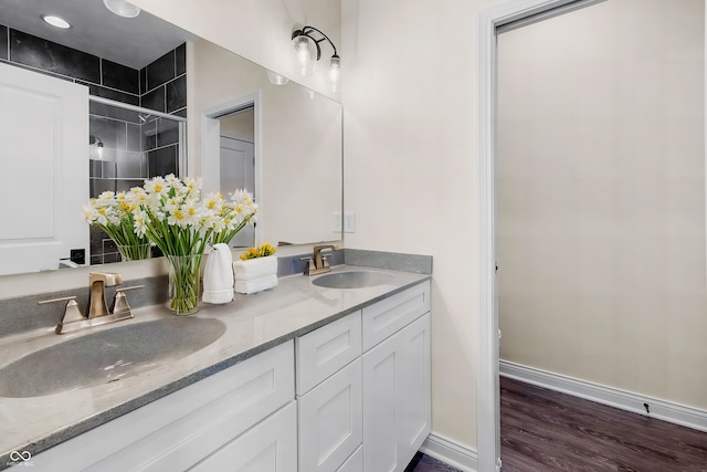 full bath featuring double vanity, a stall shower, a sink, and baseboards