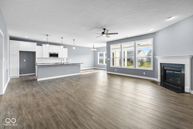 unfurnished living room featuring dark wood-style floors, a glass covered fireplace, a textured ceiling, baseboards, and ceiling fan with notable chandelier