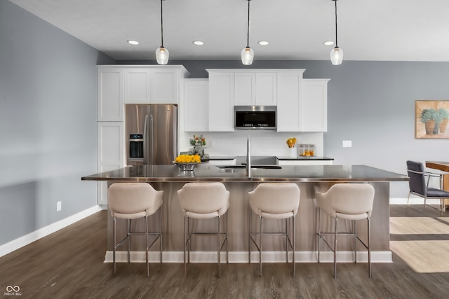 kitchen with stainless steel appliances, dark countertops, dark wood-style flooring, and a kitchen island with sink