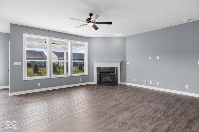 unfurnished living room featuring a ceiling fan, a glass covered fireplace, dark wood finished floors, and baseboards