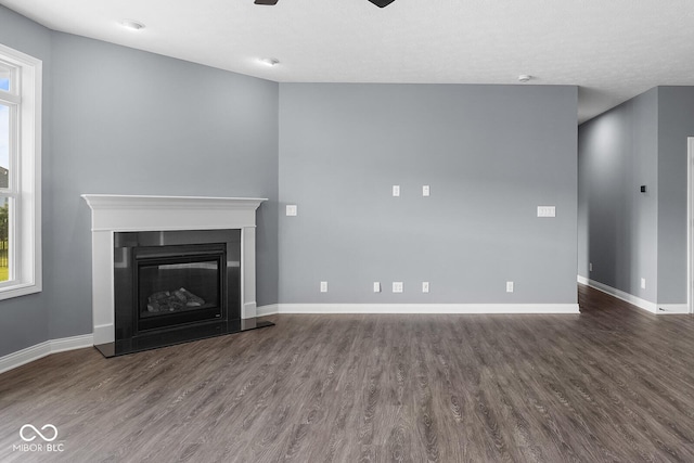 unfurnished living room with dark wood-type flooring, a glass covered fireplace, a ceiling fan, and baseboards