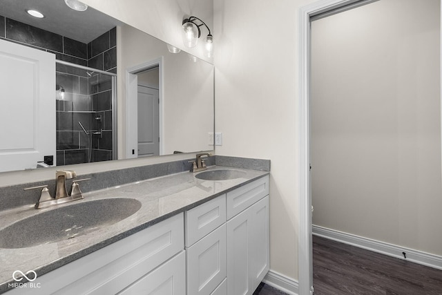 bathroom with double vanity, a shower stall, baseboards, and a sink