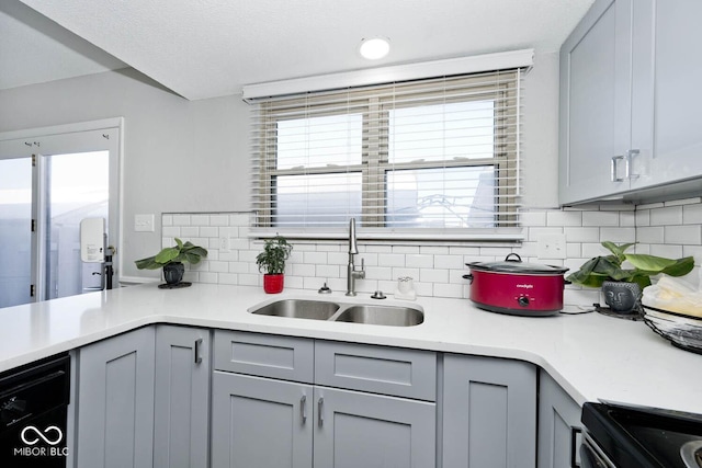 kitchen with gray cabinets, black dishwasher, tasteful backsplash, and sink