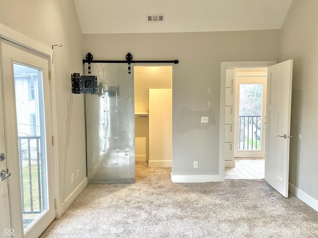 unfurnished bedroom featuring access to outside, a barn door, light colored carpet, and multiple windows