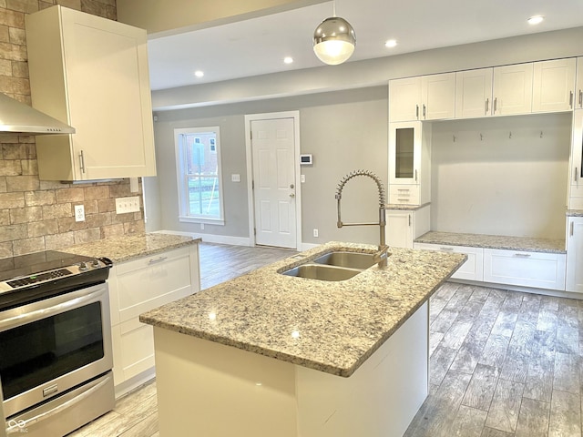 kitchen with pendant lighting, stainless steel range with electric cooktop, white cabinetry, sink, and a center island with sink