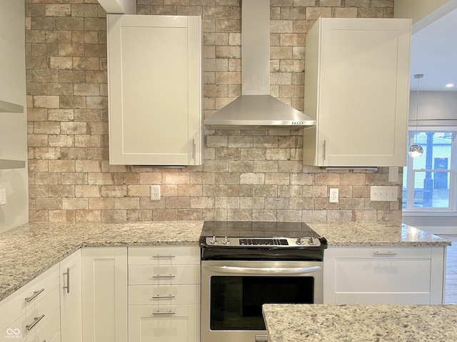 kitchen with light stone countertops, white cabinets, wall chimney range hood, electric stove, and backsplash