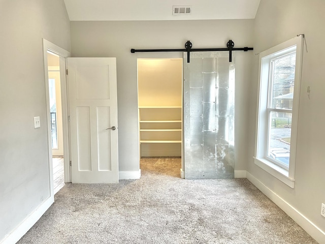 unfurnished bedroom featuring a closet, a walk in closet, a barn door, and multiple windows