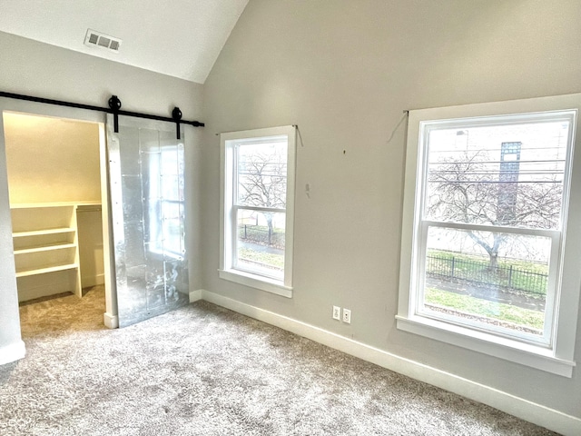 unfurnished bedroom featuring light carpet, lofted ceiling, a barn door, and multiple windows