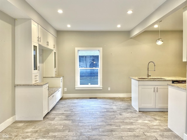 kitchen with decorative light fixtures, light stone countertops, sink, and white cabinetry