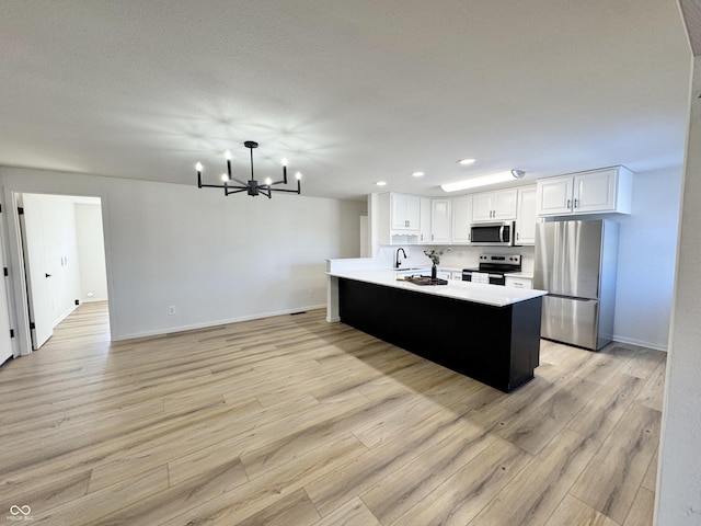 kitchen featuring an inviting chandelier, pendant lighting, stainless steel appliances, light hardwood / wood-style floors, and white cabinets