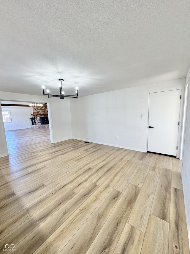 unfurnished room featuring a chandelier, a textured ceiling, and light hardwood / wood-style floors