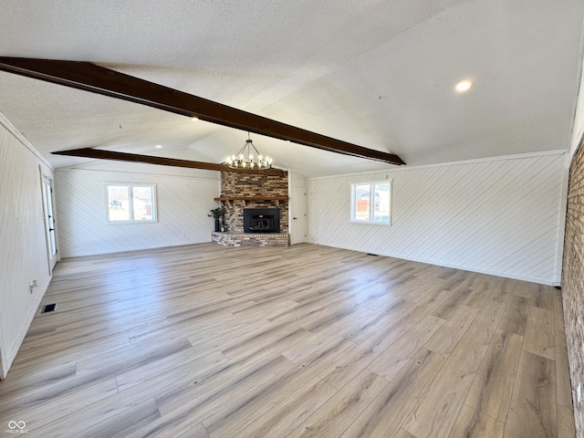 unfurnished living room with a fireplace, light hardwood / wood-style flooring, a textured ceiling, and vaulted ceiling with beams