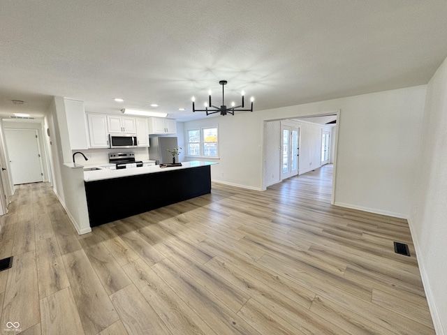 kitchen with sink, hanging light fixtures, stainless steel appliances, light hardwood / wood-style floors, and white cabinets