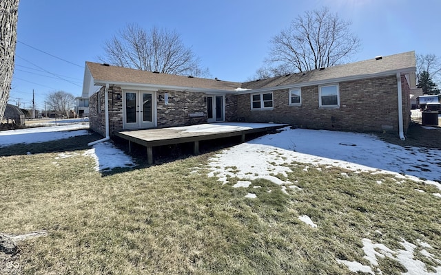 snow covered rear of property with a wooden deck, a lawn, and french doors