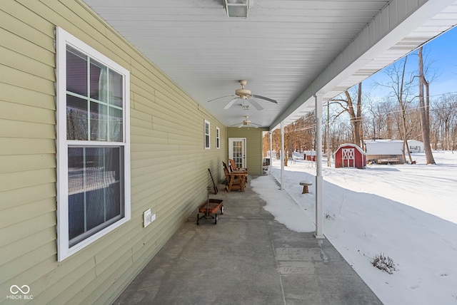 snow covered patio with ceiling fan and a storage unit