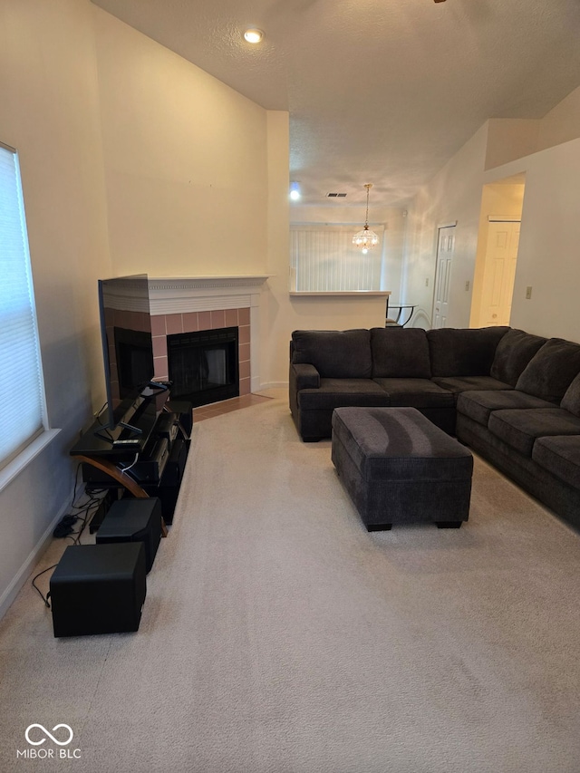 living room with a tile fireplace, a textured ceiling, a chandelier, and carpet floors