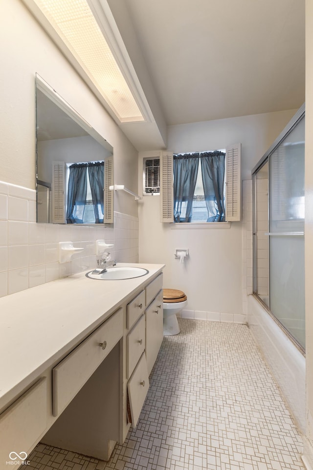 full bathroom with tile walls, enclosed tub / shower combo, vanity, toilet, and tile patterned floors