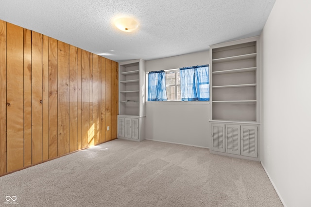 unfurnished room featuring light colored carpet, wooden walls, and a textured ceiling