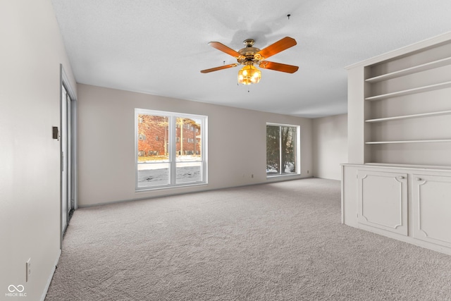 spare room featuring ceiling fan, light colored carpet, built in shelves, and a textured ceiling