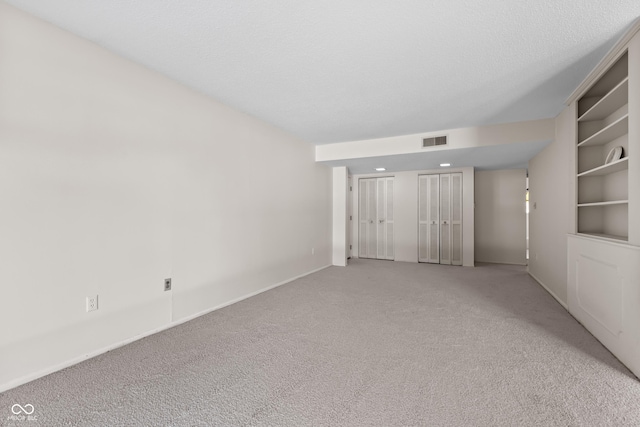 unfurnished room with light carpet, built in shelves, and a textured ceiling