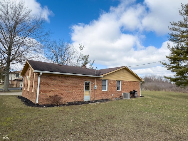 rear view of house with brick siding, a lawn, a chimney, and central AC unit