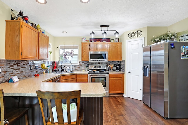 kitchen with sink, tasteful backsplash, dark hardwood / wood-style flooring, kitchen peninsula, and appliances with stainless steel finishes