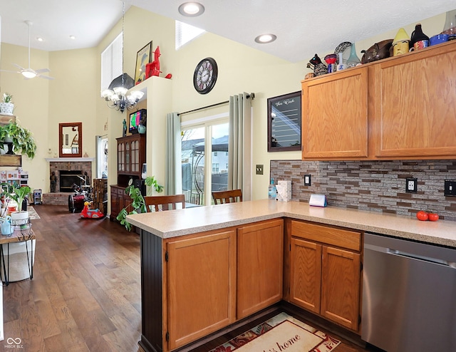 kitchen with kitchen peninsula, dark hardwood / wood-style flooring, tasteful backsplash, stainless steel dishwasher, and ceiling fan with notable chandelier