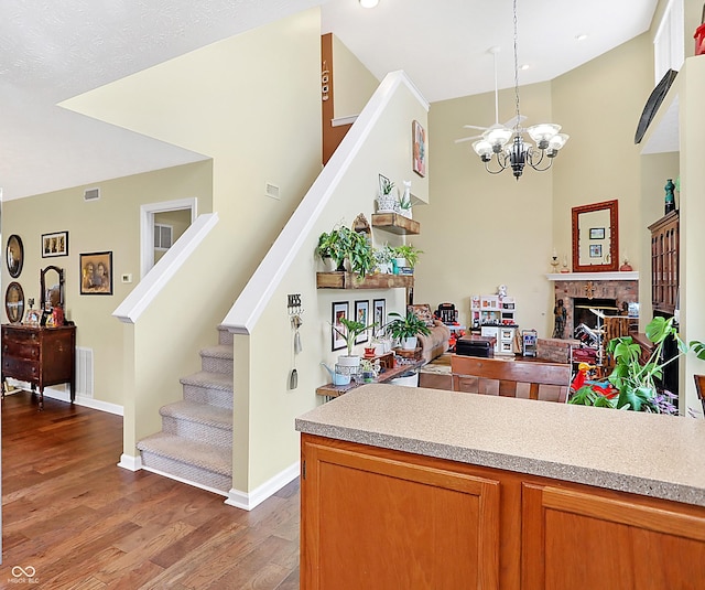 kitchen with pendant lighting, a high ceiling, an inviting chandelier, a brick fireplace, and wood-type flooring