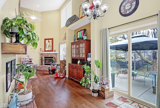 interior space with ceiling fan with notable chandelier, a towering ceiling, a fireplace, and dark wood-type flooring