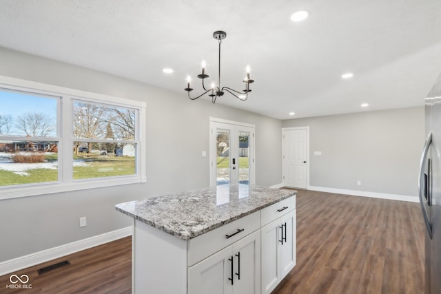 kitchen with a healthy amount of sunlight, white cabinetry, hanging light fixtures, light stone countertops, and dark wood-type flooring