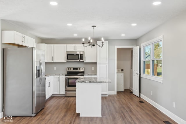 kitchen with stainless steel appliances, white cabinets, a kitchen island, washer / clothes dryer, and decorative light fixtures