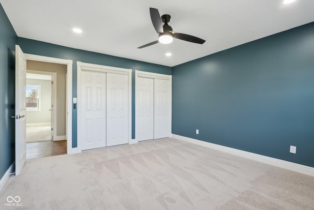 unfurnished bedroom with light carpet, ceiling fan, and multiple closets