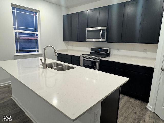 kitchen with light stone countertops, appliances with stainless steel finishes, hardwood / wood-style flooring, a kitchen island with sink, and sink