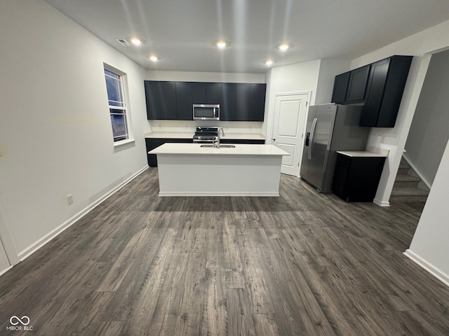 kitchen with sink, a kitchen island with sink, appliances with stainless steel finishes, and dark wood-type flooring