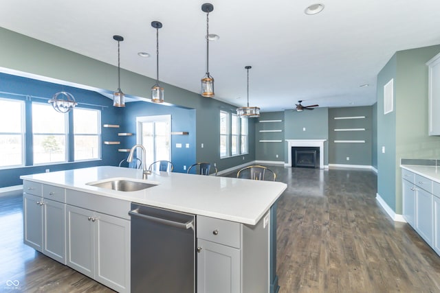 kitchen featuring dark hardwood / wood-style flooring, stainless steel dishwasher, ceiling fan, sink, and an island with sink