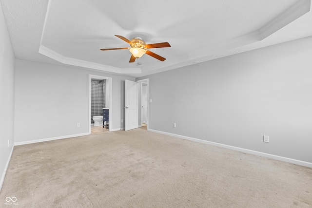 unfurnished bedroom with a tray ceiling, connected bathroom, ceiling fan, and light carpet