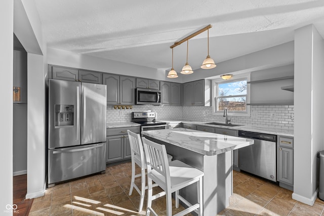 kitchen featuring gray cabinetry, a center island, backsplash, sink, and stainless steel appliances