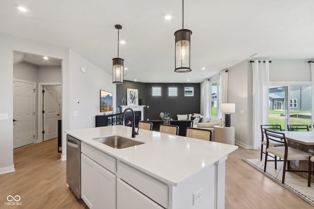 kitchen with stainless steel dishwasher, sink, decorative light fixtures, a center island with sink, and white cabinets