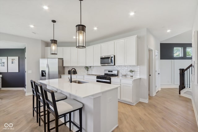 kitchen with sink, an island with sink, decorative light fixtures, white cabinets, and appliances with stainless steel finishes