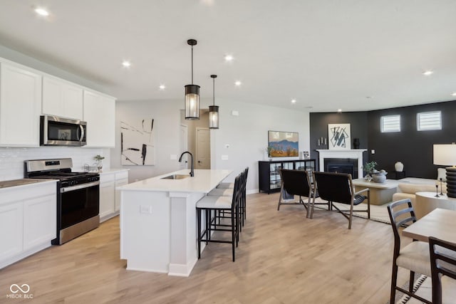 kitchen featuring appliances with stainless steel finishes, a kitchen island with sink, sink, decorative light fixtures, and white cabinets