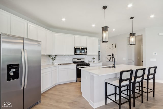 kitchen featuring white cabinets, sink, an island with sink, appliances with stainless steel finishes, and decorative light fixtures