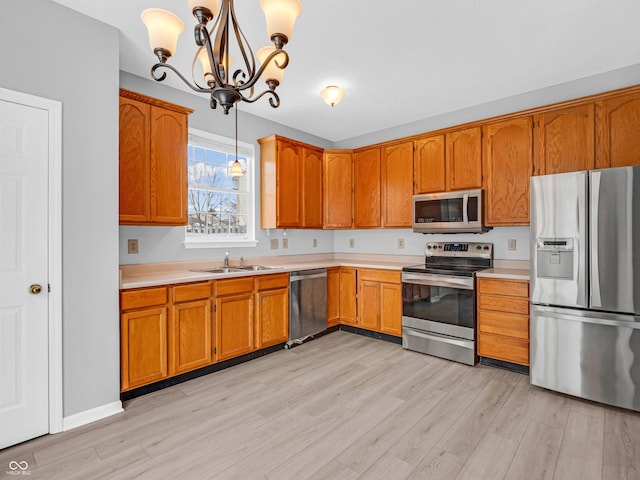 kitchen with light wood-type flooring, stainless steel appliances, sink, pendant lighting, and an inviting chandelier